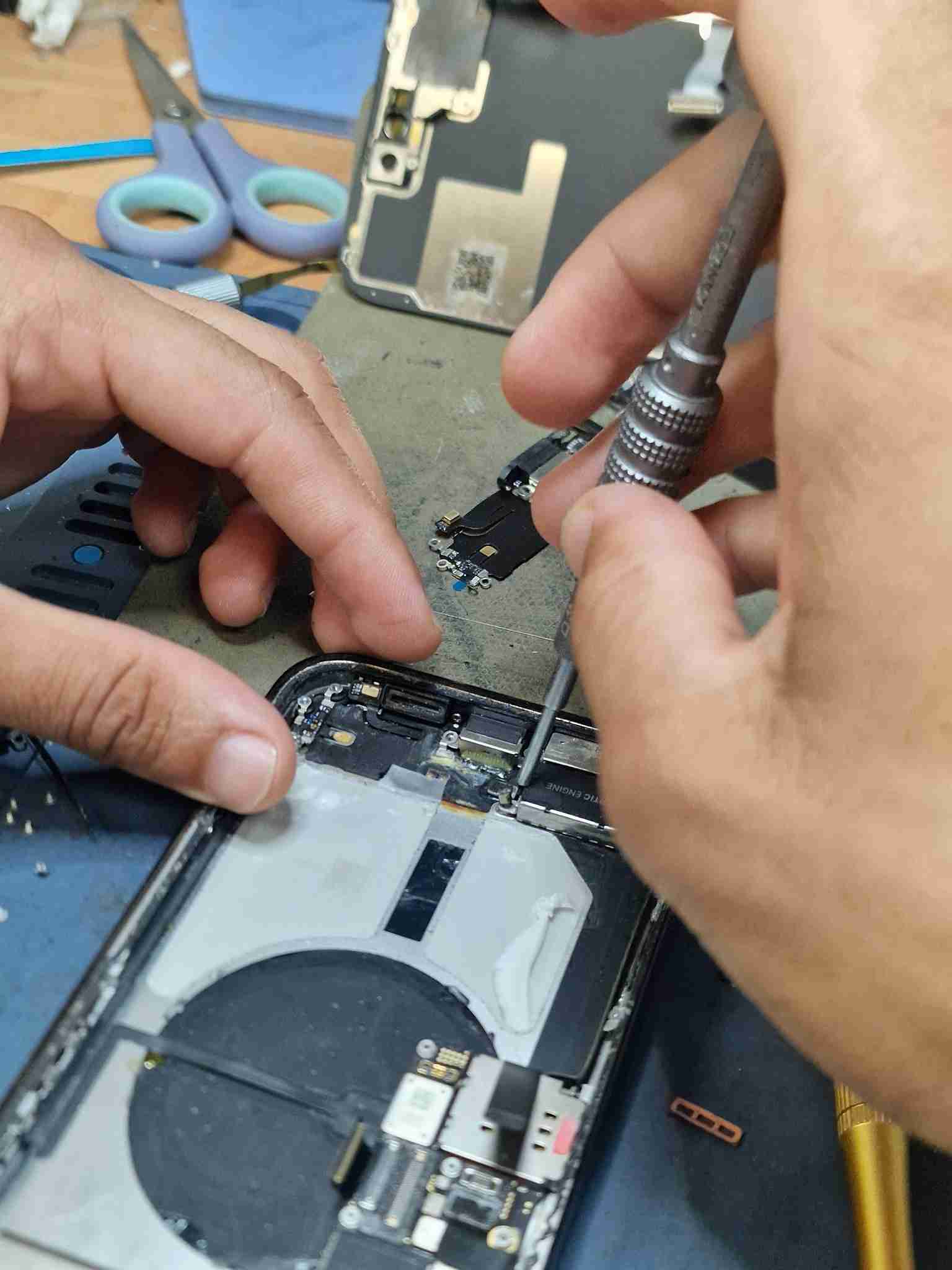 Técnico da Reparação Mobile a intervir num iPhone 14 Pro Max com danos de água, substituição do módulo de carga e tratamento interno